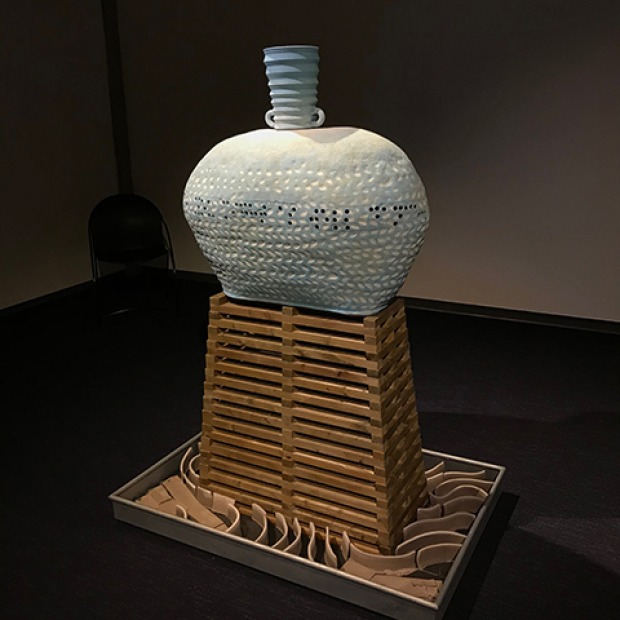 A ceramic sculpture by Iowa artist Ingrid Lilligren that resembles a ceramic vase standing on a wood-like scaffolding. 