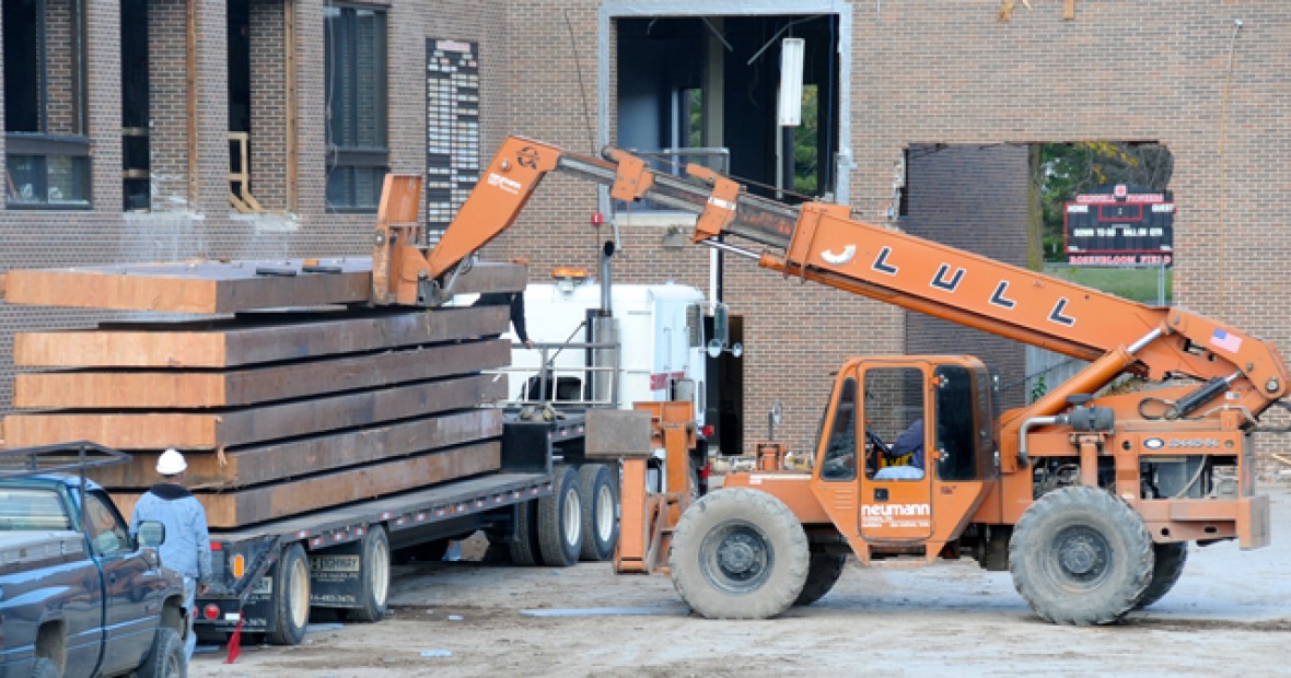 Huge sections of laminated wood are stacked on the back of a semi using heavy equipment