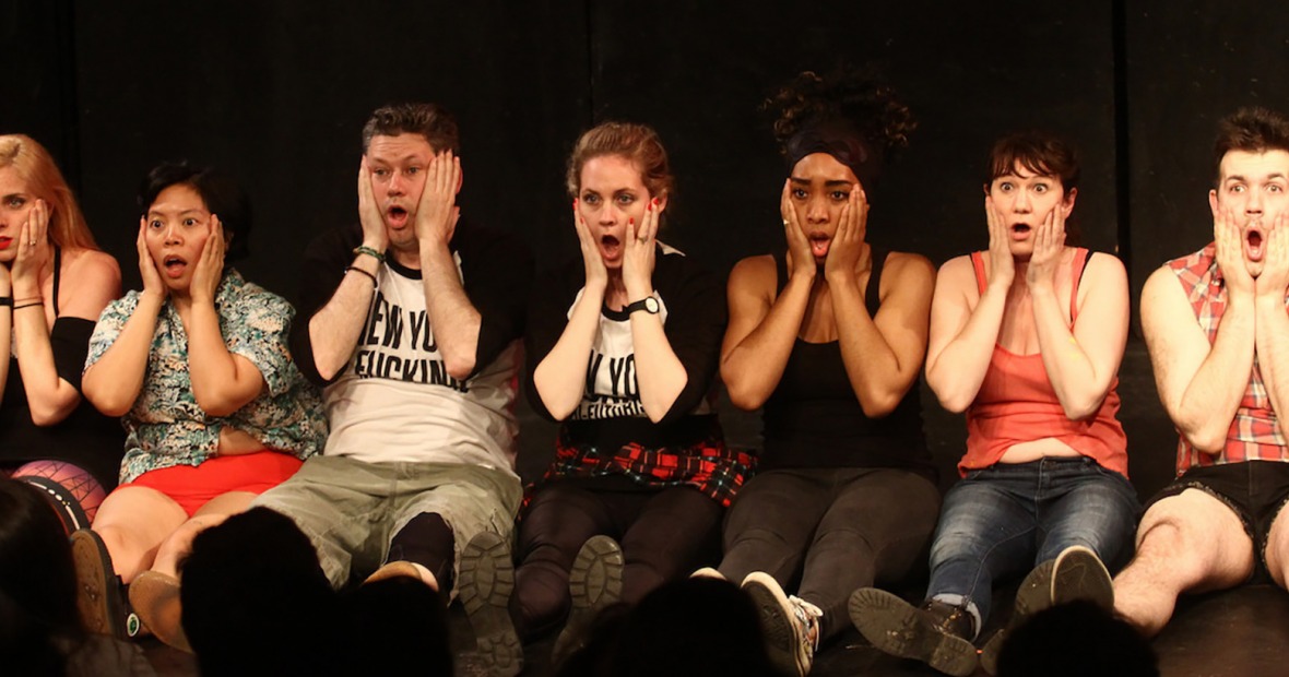 Neofuturists sitting on the floor in a row with surprised expressions