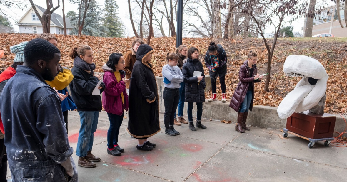 Students and Professor Lee Running critique a sculpture in an outdoor space