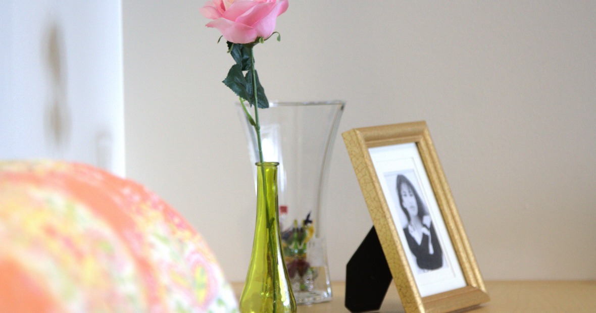 a vase with a singular flower next to a framed photo of Selena Quintanilla