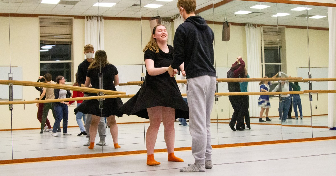 A student in a black dress dances with another student