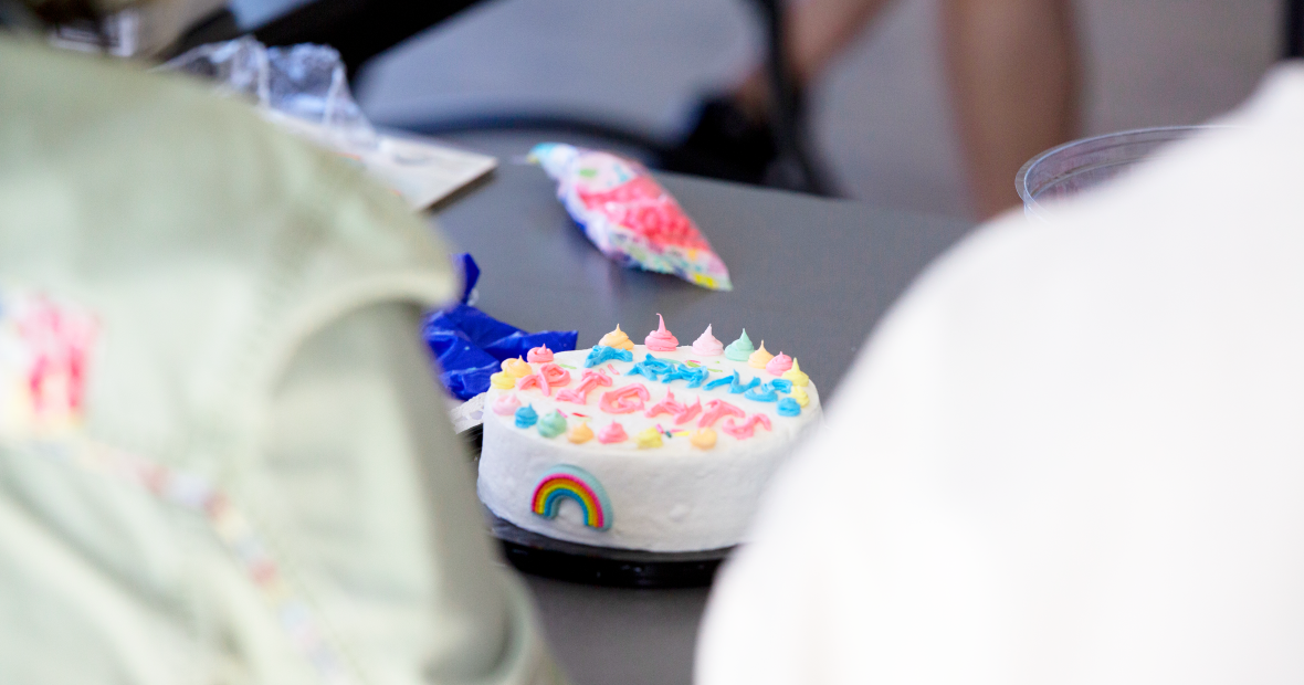A white cake with the words, "Trans Rights" with a rainbow and colorful frosting tips.