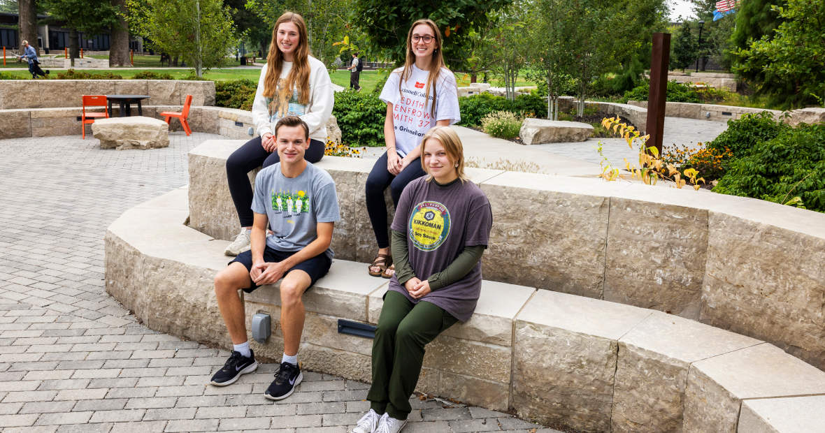 Four students sit on a gray brick ledge.