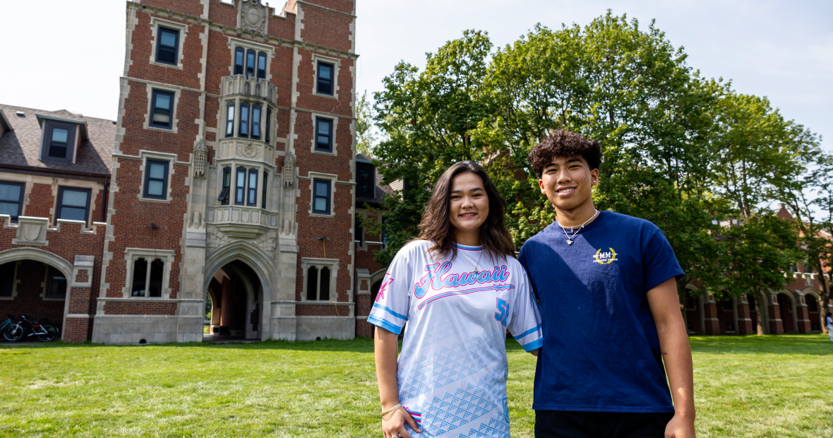 Kylie Ann Smith '27 and Preston Yoshida '27 stand in a green Mac Field in front of a looming Gates Tower.