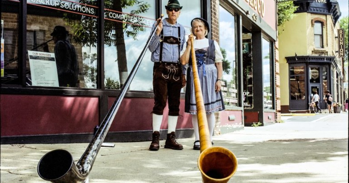 A picture of two yodelers holding large saxophone like instruments. The angle begins at the horn of the instrument.