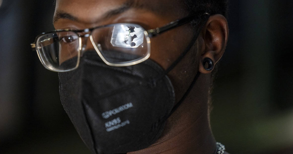 A close up of a masked Black student with glasses. Their glasses reflect the shadows of two squirrels.