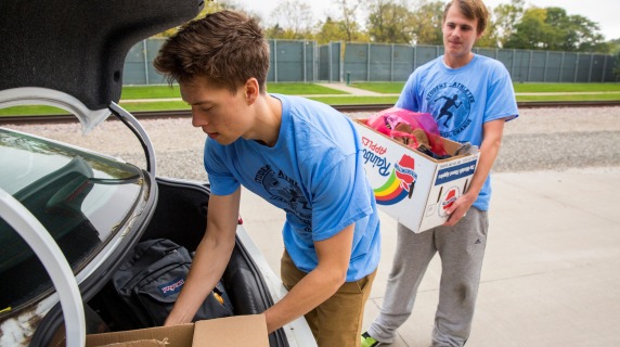 Members of Student Athletes Leading Social Change load donations into the trunk of a car