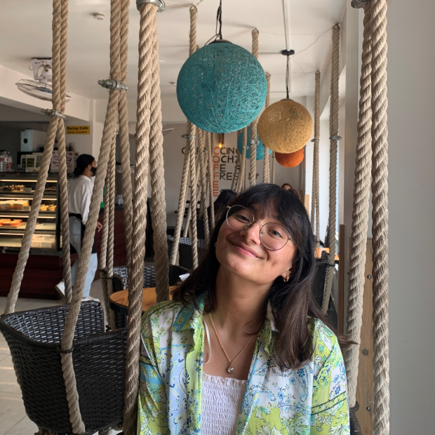 Diya Shrestha, sitting in café surrounded by colorful twine balls and swings hanging from the ceiling