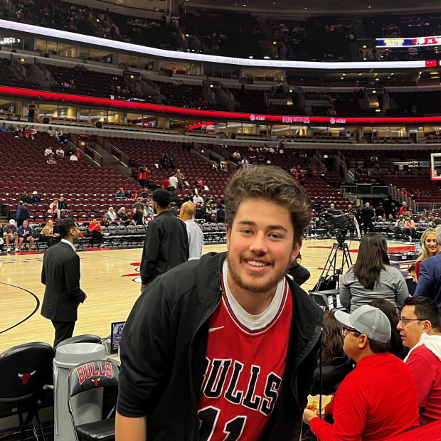 Jeronimo Camargo smiling in front of a basketball court with the Chicago Bulls basketball team symbol on a screen above his head