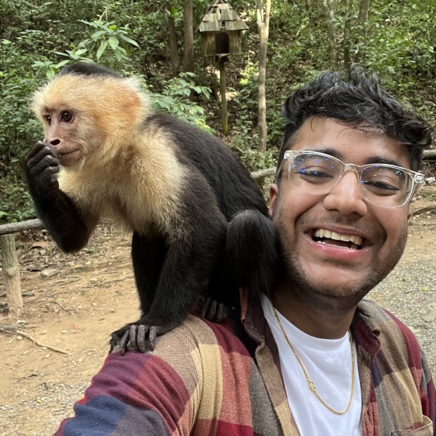 Shrey Agrawal smiling at the viewer with a monkey on his shoulder with green trees in the background