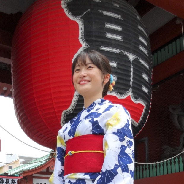 Yuina Iseki wearing a blue, yellow, white and red kimono and standing in front of a large red lantern