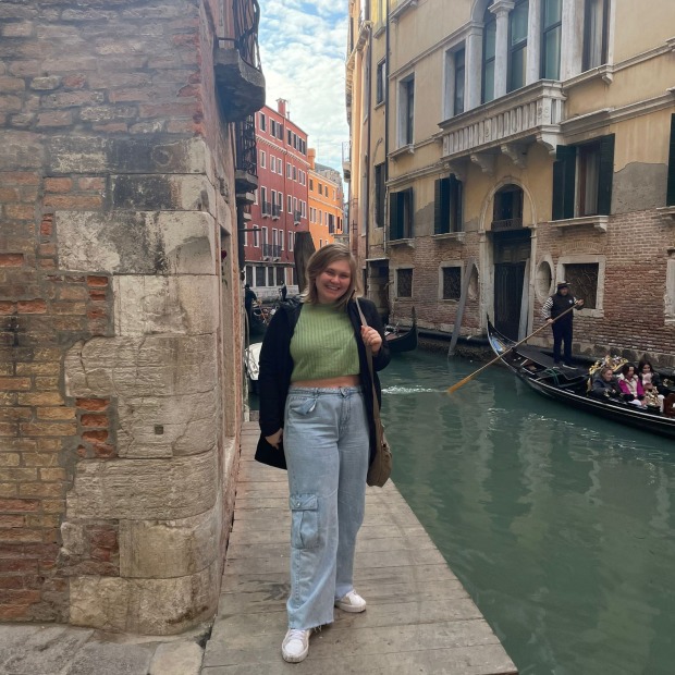 Bailey Sowers stands at a building corder with a canal and gondola in the background
