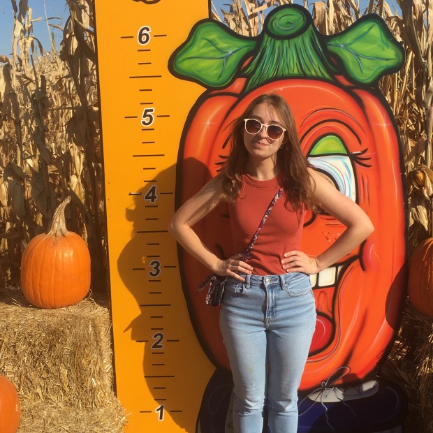 Madeline Fialkov standing next to pumpkin and in front of sign with height chart and large cartoon pumpkin