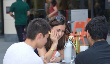 A woman faculty member visits with two students at an outdoor table.