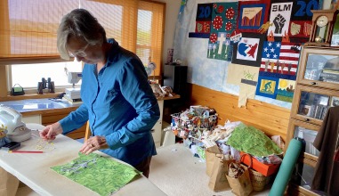 Ellen Modersohn works at a table, arranging her quilt squares
