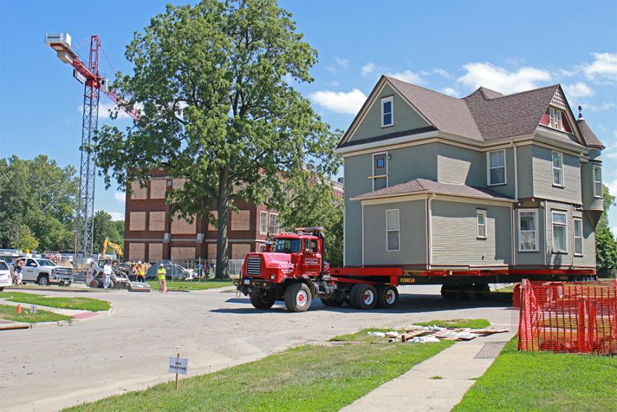 Two-story house on the back of a flat-bed truck that's turning the corner onto Park Street, looking southeast at ARH