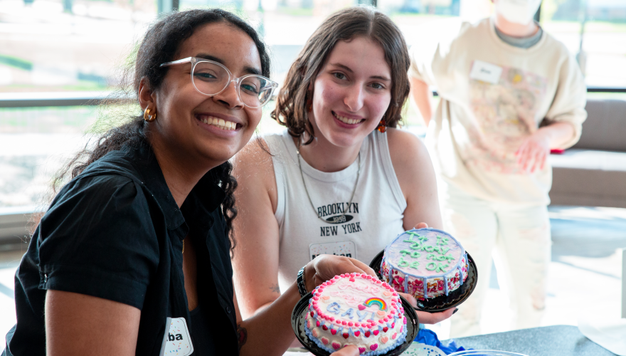 Pichardo and her friend hold their decorated cakes at the camera while smiling.
