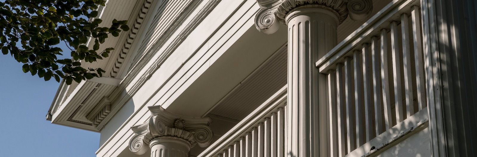 Ornamental columns and architectural details at top of an older cream-colored building with outdoor covered porch