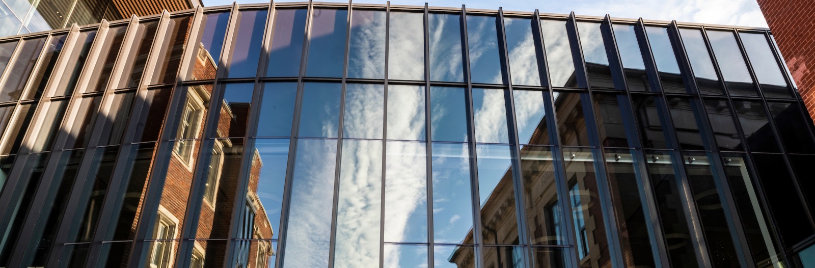 metal and glass building with the reflection of blue sky with clouds and brick and stone buildings
