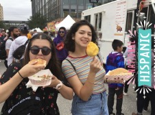 Eva and friend eating fair food at a street festival with splash on the sit that says national Hispanic heritage month