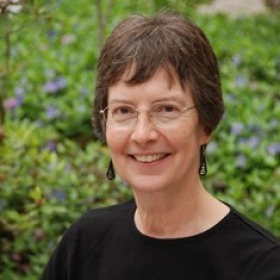 A woman with short hair, glasses and a black shirt smiles at the camera.