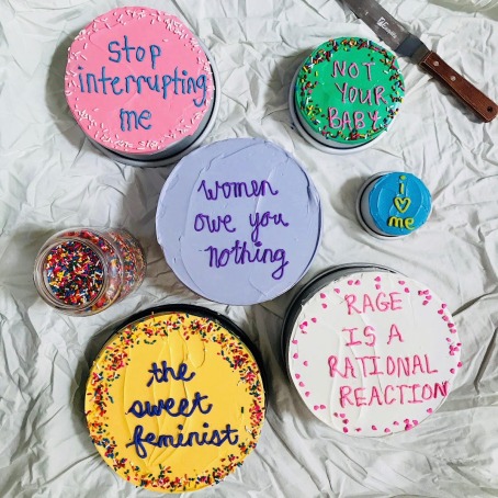 Six cakes with different frosting and decorations read varying messages, from "Women owe you nothing," and "Rage is a rational reaction."