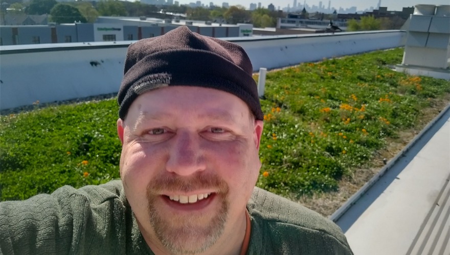 A man in a black cap takes a selfie while amidst a rooftop meadow.