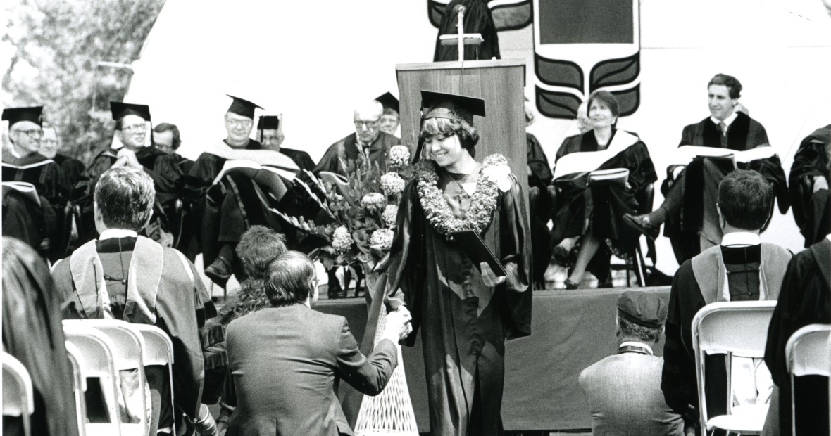A student with a flower necklace around their neck walks down the center aisle at the 1989 Commencement ceremony. Courtesy of Grinnell College Special Collections & Archives. 