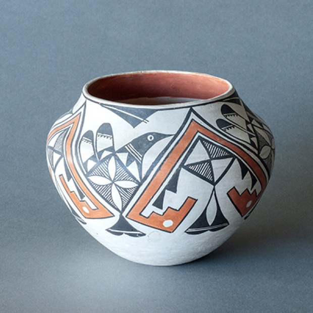 A Pueblo pot with orange and black geometric patterns and a black figure of a bird against a gray background.