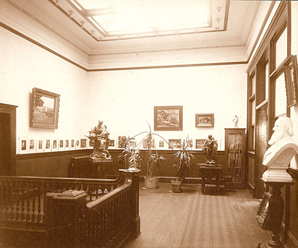 Interior of Carnegie Library second floor showing large plants, several large and small pieces of art, and the balustrade to the stairs.