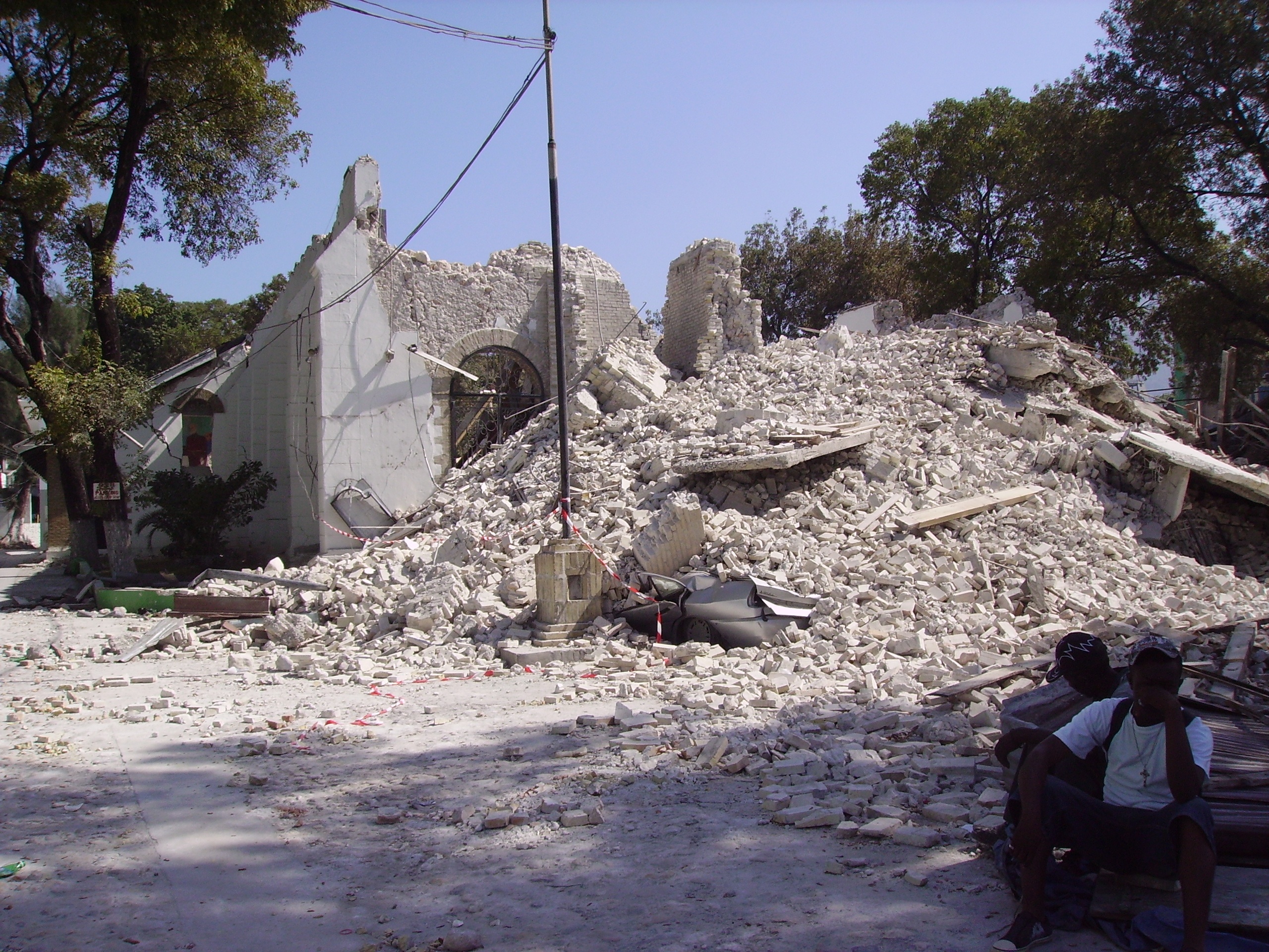 Pile of finely broken rubble in front of partially standing wall with preserved glass