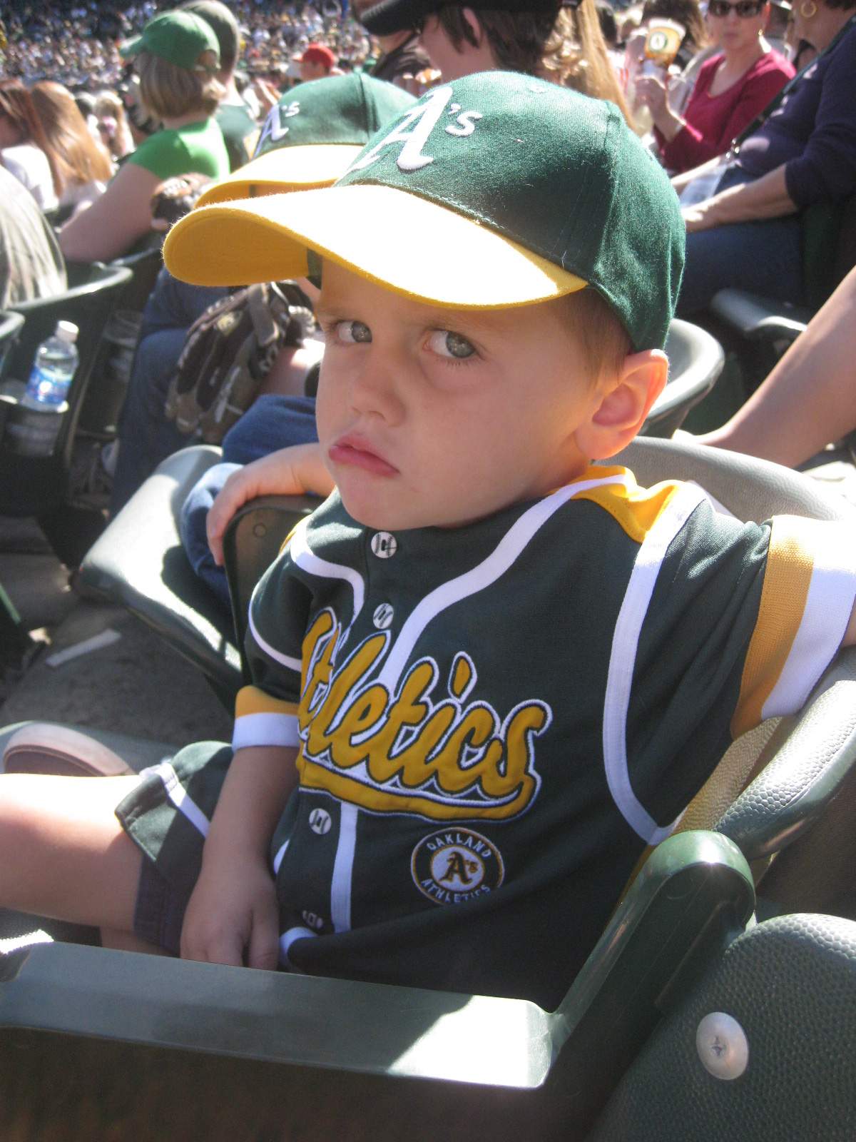 boy in A's had and shirt pouting in stands