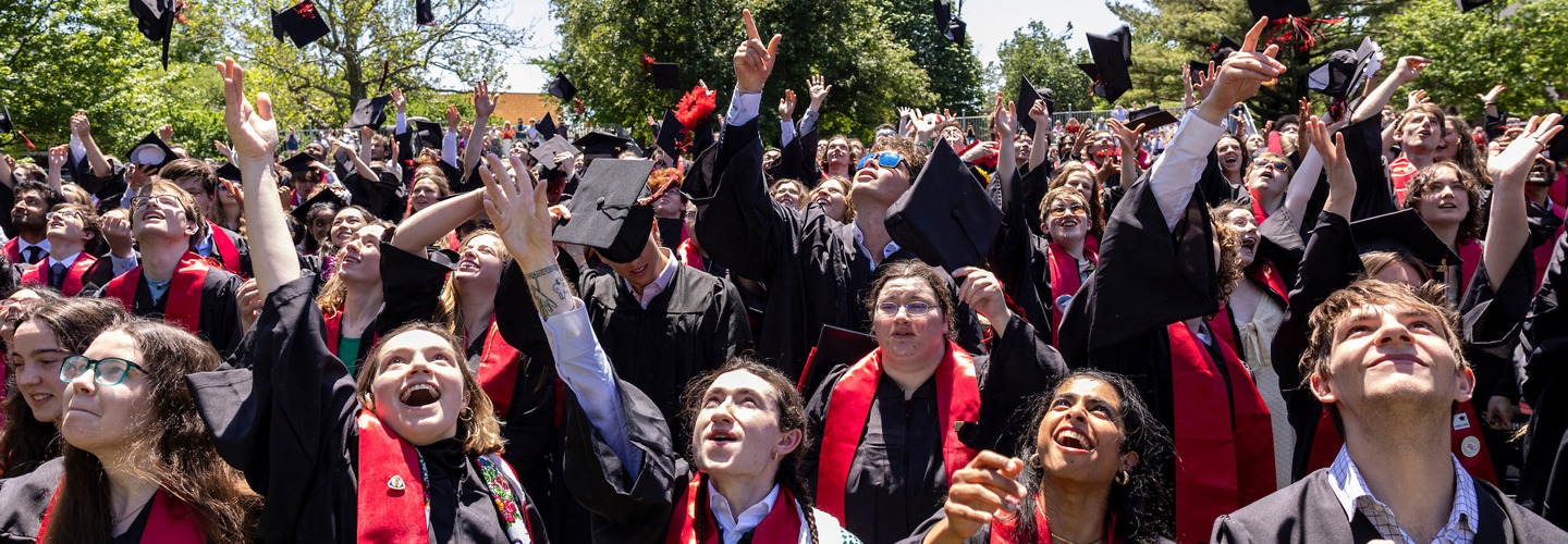 Students at Grinnell College commencement celebration toss their mortar boards in the air