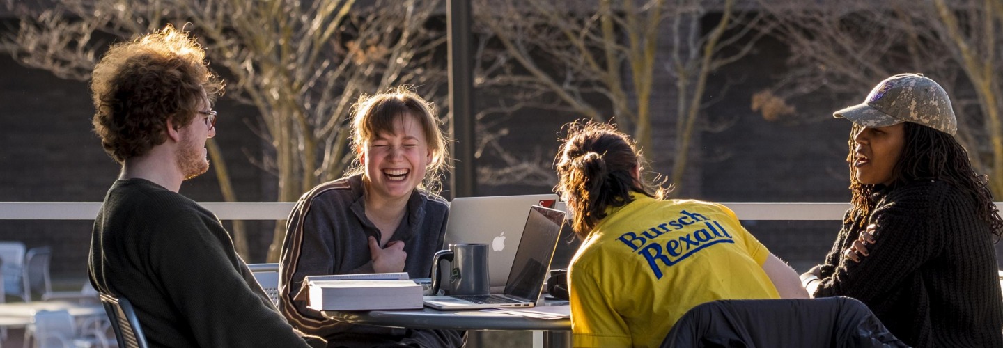 4 students laugh at an outdoor table