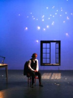 A lone performer sits in front of a window and a starry backdrop in the student-directed one-act play festival
