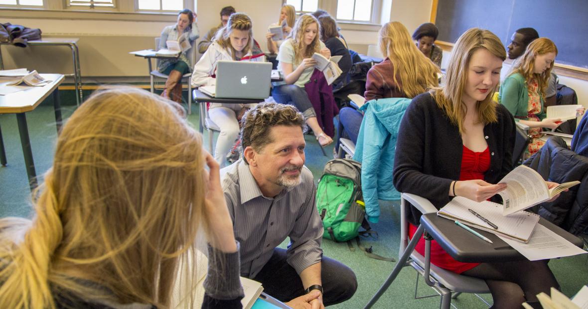 Tyler Roberts squatting next to students while teaching a course