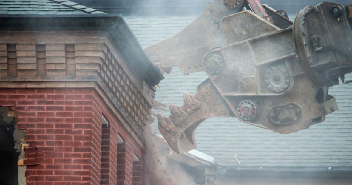 Heavy machinery kicks up a cloud of dust as it destroys part of a roof.