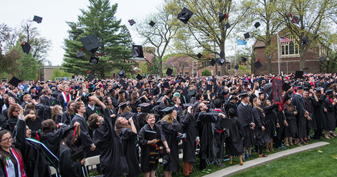 A crowd of graduates throw their caps into the air.