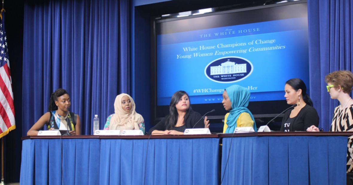Yesenia Ayala sits at a table with five other women in front of a screen reading "White House Champions of Change: Young Women Empowering Communities."