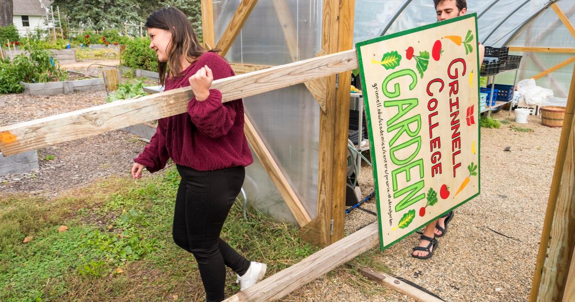 Two students carry a sign for the Grinnell College Garden