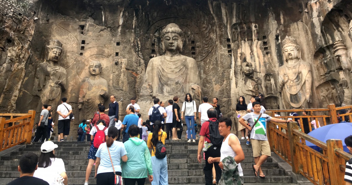 Tourists on steps in front of huge Buddha carved into a cliff