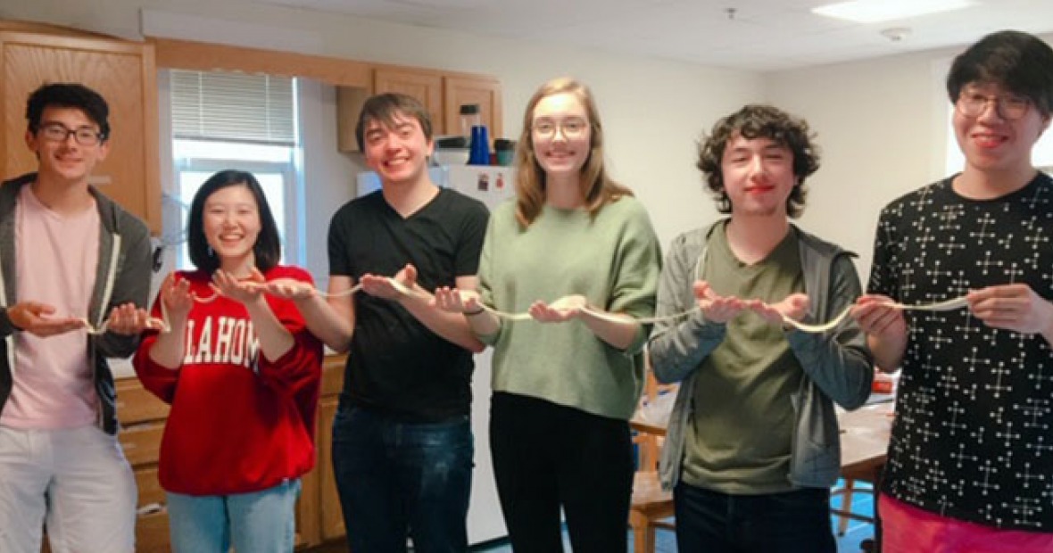 Students holding a long noodle stretched across their hands