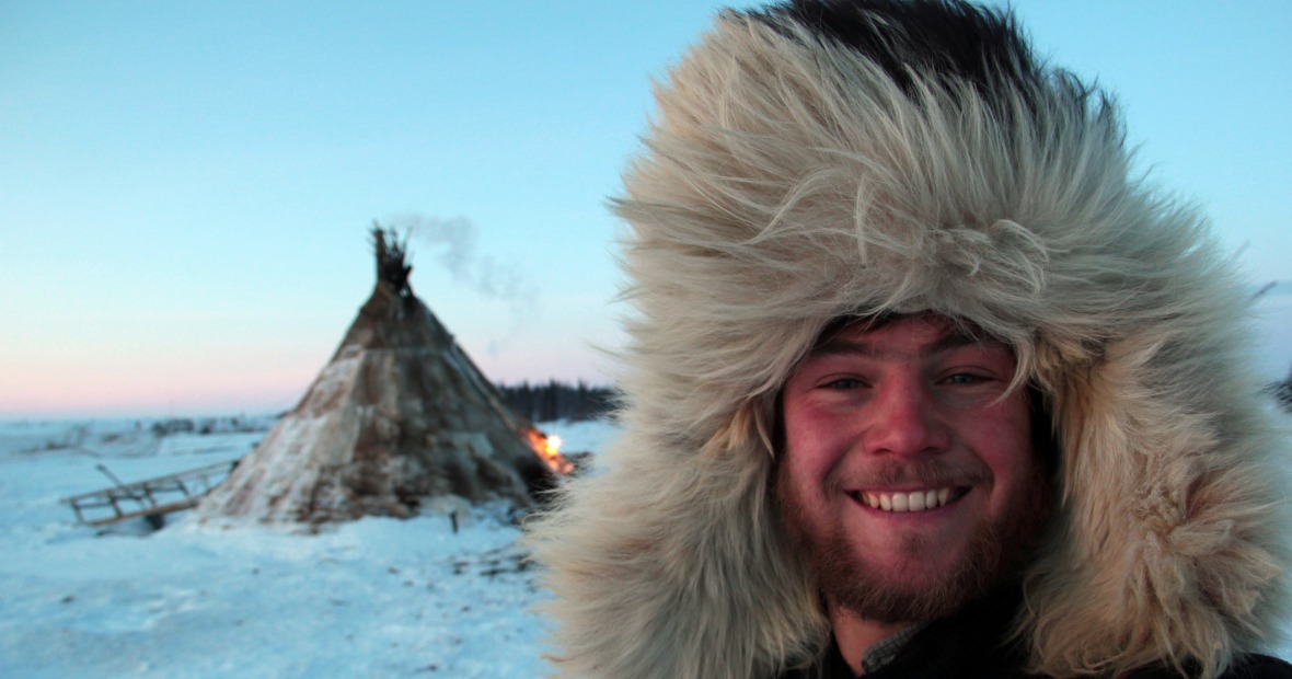 Alex Reich in the Arctic in a fur hood with a teepee structure in the background