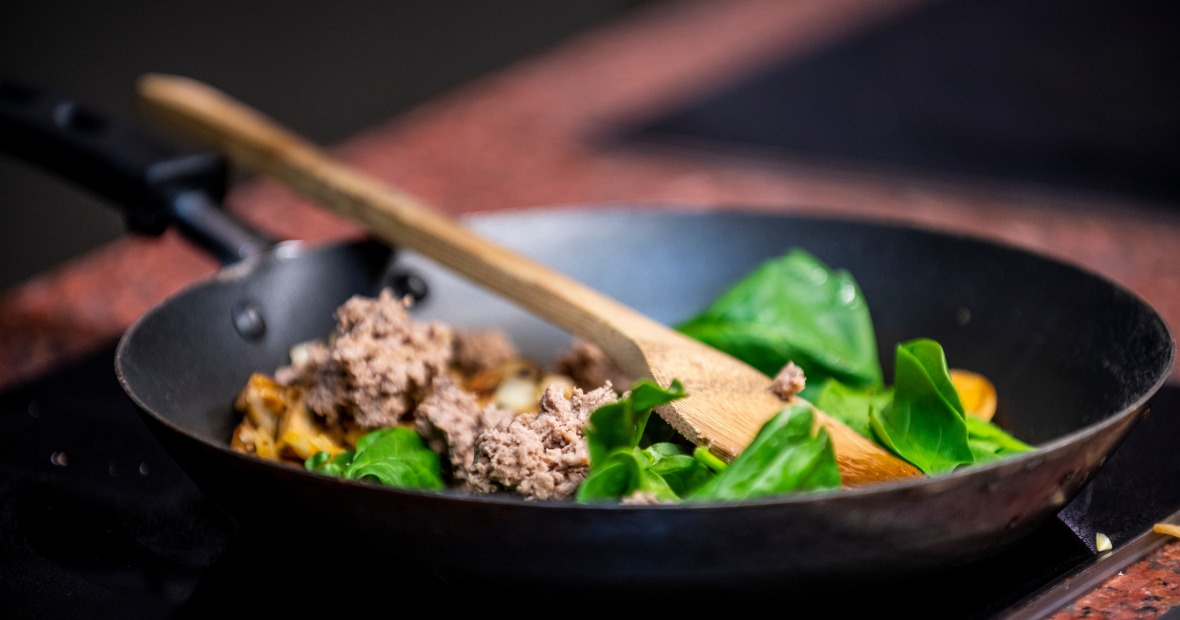 A small saute pan with fresh spinach leaves and ground meat, ready to be tossed together