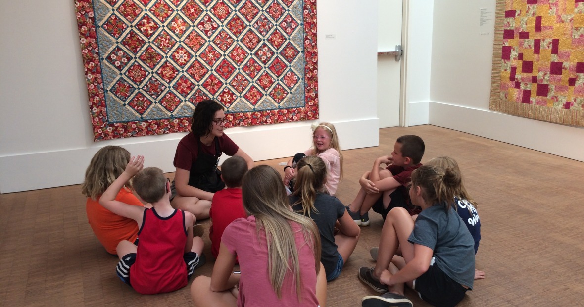 Discussion group with students seated on floor in front of a red and black quilt