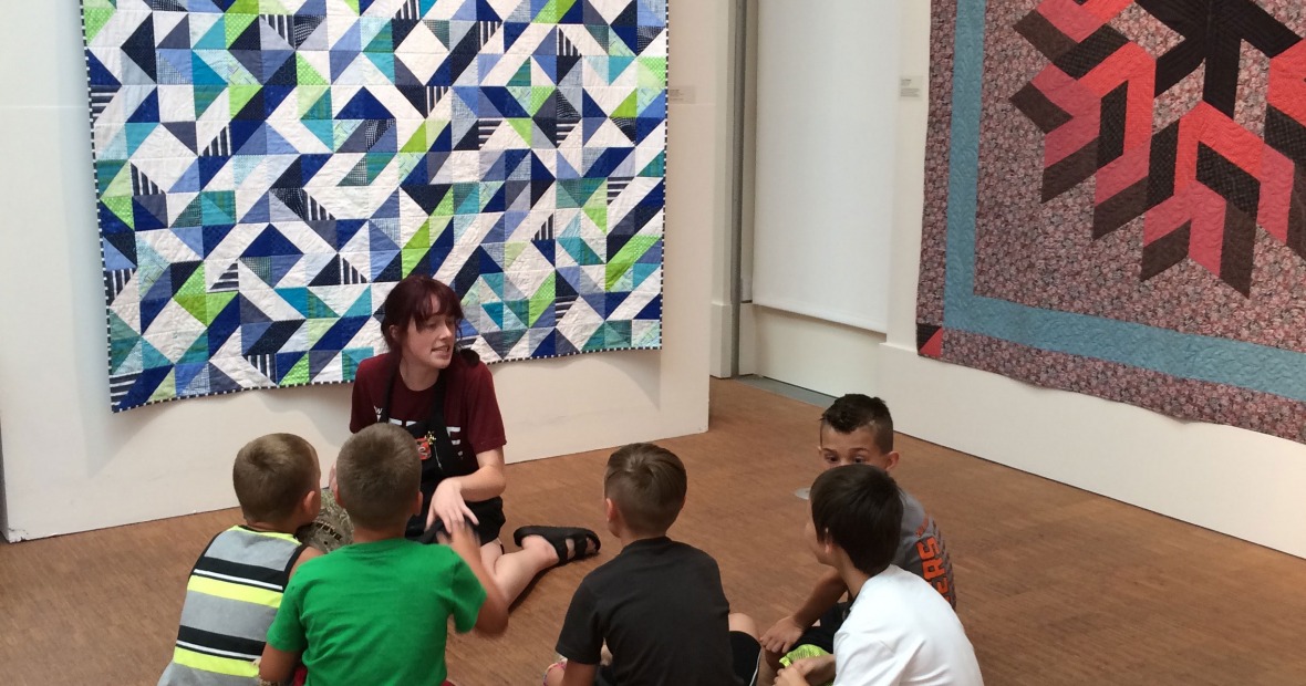 Student discussion in front of brightly colored blue, green, and white quilt