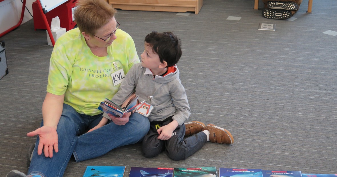 Preschool teacher sitting on floor with child looking at book