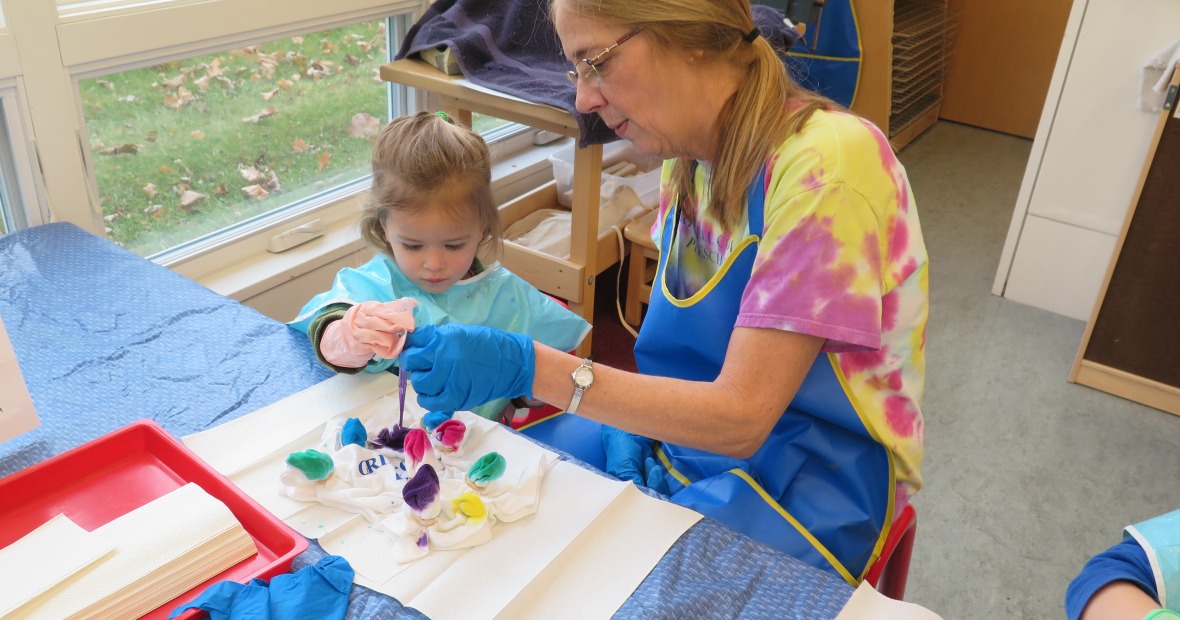 Preschool teacher helping child with tye dye t-shirt