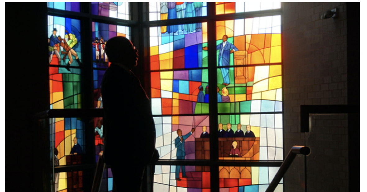 A silhouetted figure in front of stained glass